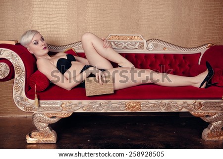 Blonde beautiful woman on red sofa wearing black bra. Cabaret style