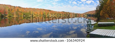 A lifeguard chair sits on the edge of Perch Lake in the Catskills with a reflected sky in Autumn in New York