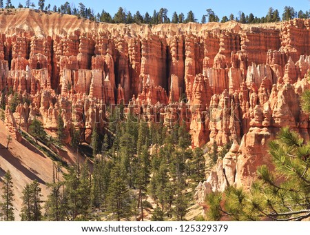A ridge of dozens of hoodoos above a valley of sand and pine trees in Bryce Canyon National Park, Utah