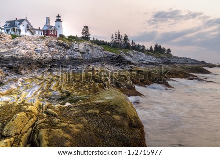 Dawn at the Pemaquid Point Light, as waves lap against intreresting layers of rock formations, on the mid coast of Maine