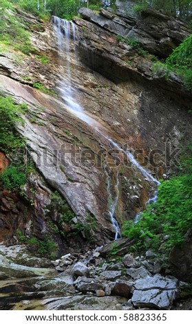 A creek emerges from the forest above to plunge over a slanted rock cliff and slowly low down the face at upper Nevele Falls near Ellenville, NY in the Shawangunk Mountains of New York