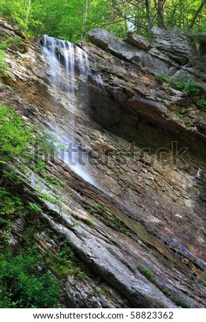 A creek emerges from the forest above to plunge over a slanted rock face at upper Nevele Falls near Ellenville, NY in the Shawangunk Mountains of New York