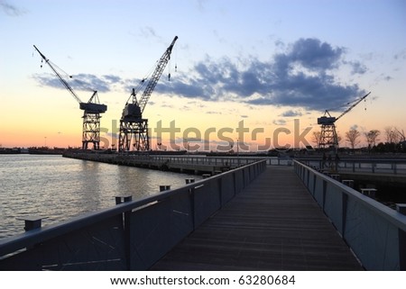 Three cranes and a boardwalk pier silhouetted against the sunset in the harbor at Erie Basin Park at Red Hook Brooklyn - Brooklyn, NY