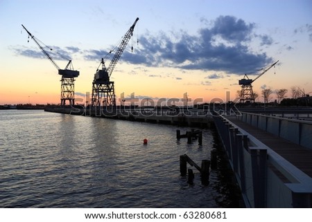 Three harbor cranes on a pier silhouetted against the sunset in the harbor at Erie Basin Park at Red Hook Brooklyn - Brooklyn, NY