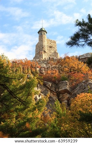 Skytop Tower rises above an Autumn tree covered-cliff above Mohonk Lake in the Mohonk Preserve in the Shawangunk Mountains of New York