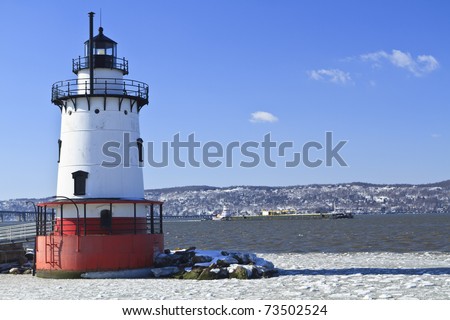 A barge head sup the icy Hudson River behind the Sleepy Hollow Lighthouse