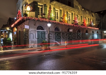 Tail lights streak by a building on the corner of Barrcks St and French Market Place festooned with Christmas decorations in the French Quarter of New Orleans