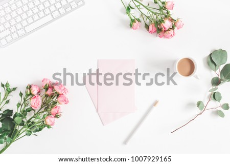 Office desk with computer, rose flowers, eucalyptus branch, pink paper blank. Flat lay, top view, copy space.