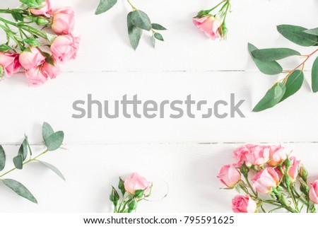 Flowers composition. Frame made of eucalyptus branches and pink rose flowers on white wooden background. Flat lay, top view, copy space.