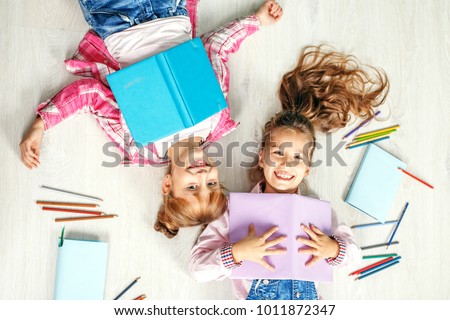 Two funny little girls with books. Flat lay. The concept of childhood, learning, friendship, family, school, lifestyle.