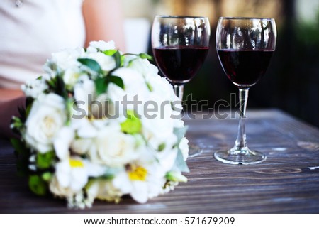 A bouquet of flowers and two glasses of wine on a wooden table. The concept of wedding and celebration.