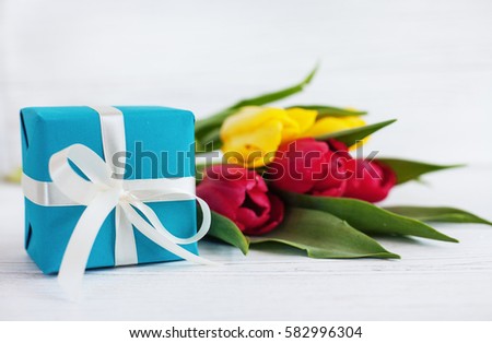 White wooden background, tulips and blue gift. Concept of holiday, birthday, Easter, March 8.