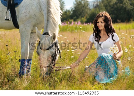 Beautiful girl walks on white horse on a summer meadow