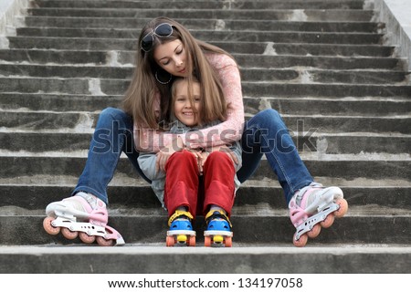 A young mother with her daughter sitting on the stairs in the Park with roller skates