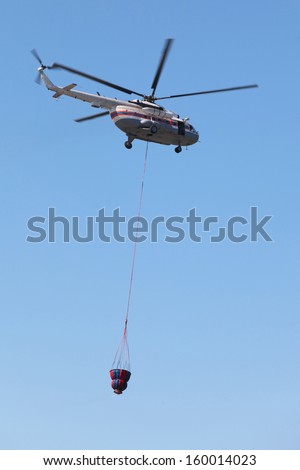 Fire helicopter with the reservoir for water flies on the background of blue sky