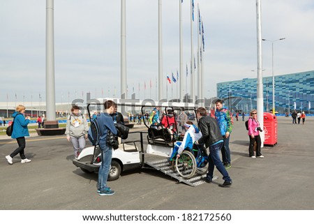 SOCHI, RUSSIA - MAR 8, 2014: Olympic Park. The young man helps the disabled in wheelchairs to enter the electric car is equipped for people with disabilities.