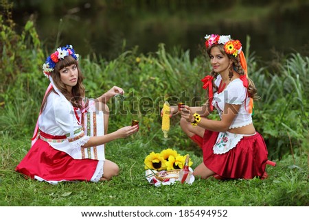 Two girls in Ukrainian costumes dressed for the holiday of Ivan Kupala sitting on the Bank of the river and drink vodka