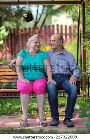 Happy elderly couple sitting on a bench in a country yard