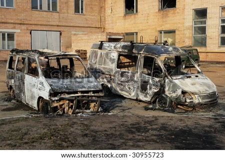 Two burnt down motor vehicles against a city landscape