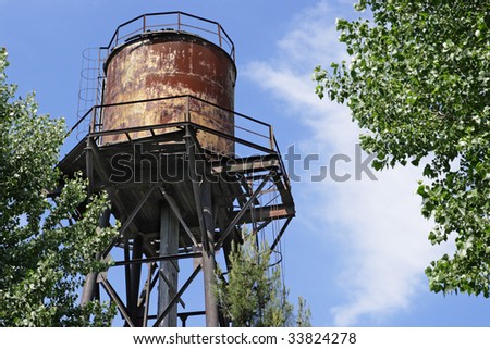 Old metal rusty water tower against the blue sky and tree branches