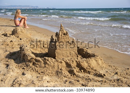 The sand castle on seacoast and the girl sitting on sand in the distance