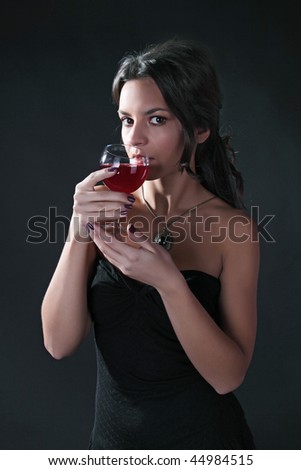 The fine woman in an evening dress with a wine glass on a black background