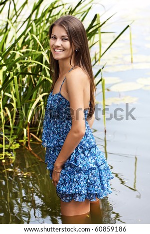 The girl in a dark blue dress stand knee-deep in water on lake