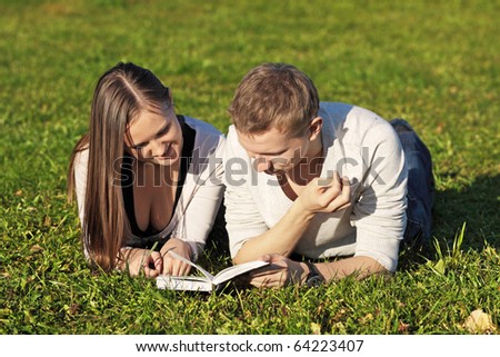 The guy and the girl lie in park on a grass with the book