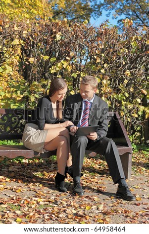 The guy and the girl sit on a bench in autumn park with the laptop