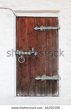 Old wooden door with shod door hingeds against a white brick wall