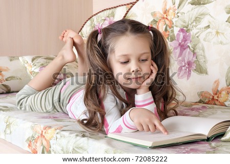The little girl lies on a sofa and reads the book