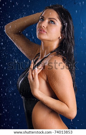 Portrait of the sexual young girl in a bathing suit in water splashes on a dark blue background
