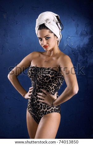 The wet girl in a bathing suit with a towel on a head against a dark blue wall