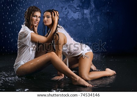Two wet semiundressed sexy girls on a dark blue background in water splashes