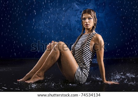Portrait of the sexual young girl in a striped vest in water splashes on a dark blue background