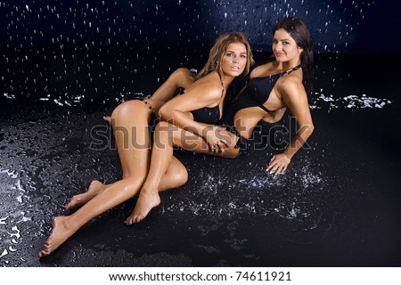 Two sexy girls in bathing suits embrace in water splashes