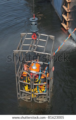 A man in a diving equipment, lift up out of the water in a special cage