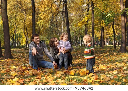 A family with two children walking in the autumn park among the fallen leaves