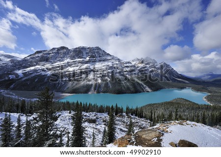 Sapphire-blue of star-shaped Peyto Lake blinking white-grey snowy mountains rimmed with white clouds Banff