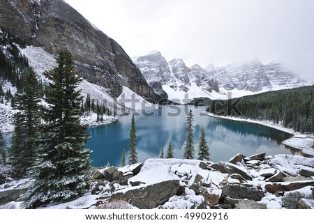 Glimmering crystal sapphire blue of Moraine Lake framed with ten snow peaks standing white-gray in morning fog Banff