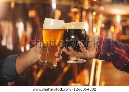 Cropped close up of two men clinking beer glasses together, celebrating at the beer pub. Professional brewers toasting with their beer glasses. Success celebration, oktoberfest festival concept