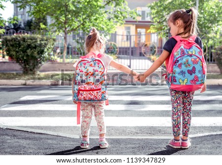 Children go to school, happy students with school backpacks and holding hands together, cross the road, the concept of education with girls
