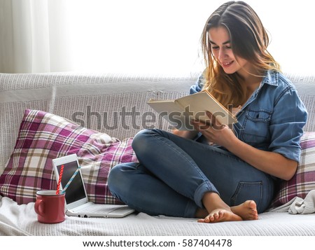 White cozy bed and a beautiful girl with a computer and a book, drinking a hot drink, concepts of home and comfort, place for text
