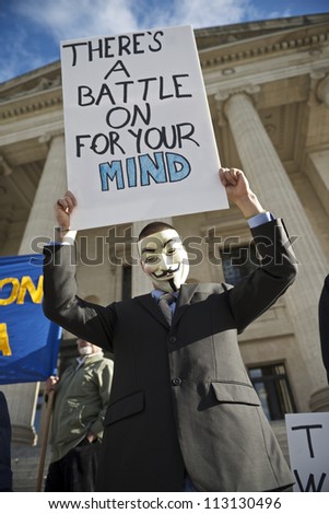 WINNIPEG, CANADA - SEPTEMBER 17: An unidentified protester wearing a Guy Fawkes mask lifts a sign while marking Occupy Wall Street\'s one year anniversary on September 17, 2012 in Winnipeg.