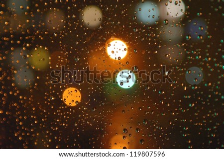 Droplets of night rain on windowpanes, on back plan washed away lights of the torches. Shallow DOF