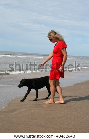 Woman in red dress and a black dog on oceanic beach. Atlantic ocean coast in Argentina.