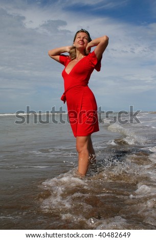 woman in red in shallow beakers under blue sky. Atlantic ocean coast in Argentina.