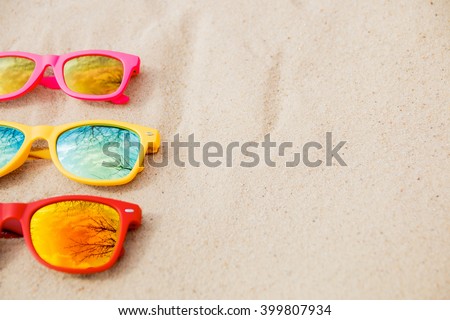 sunglasses for Family. Red, pink, yellow sunglasses on the sand background. Family sunglasses on the beach with reflection of sky and trees