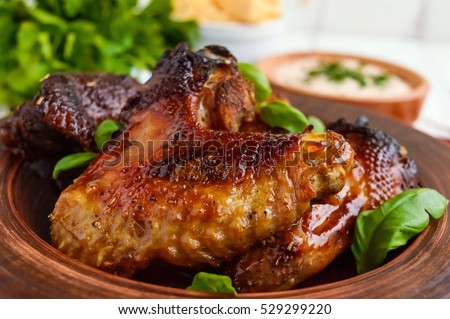 Fried wings (duck, chicken) in a honey glaze in a clay bowl on a light background.  Close up