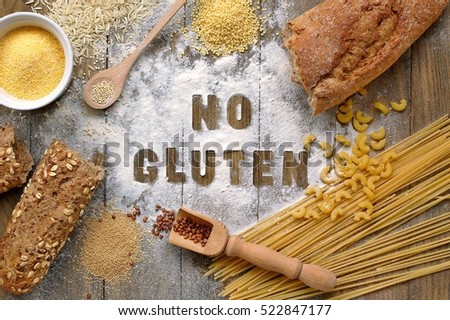 Gluten free flour and cereals millet, quinoa, corn flour polenta, brown buckwheat, basmati rice, bread and pasta with text no gluten in English language with spoon on brown wooden background,up view